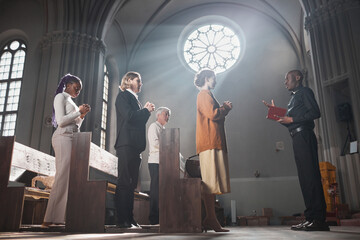 Group of people standing and praying during mass together with priest in the church
