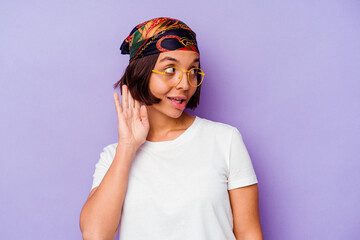 Young mixed race woman wearing a bandana isolated on purple background trying to listening a gossip.