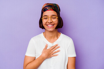 Young mixed race woman wearing a bandana isolated on purple background laughs out loudly keeping hand on chest.