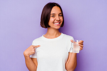 Young mixed race holding a glass of water isolated on purple background person pointing by hand to a shirt copy space, proud and confident