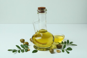 Bottle and bowl of oil, olives and twigs on white background