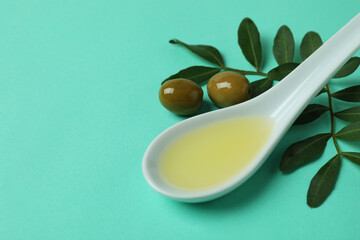 Spoon with oil, olives and twigs on mint background