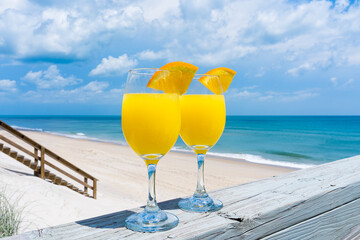 Bright yellow glasses of mimosa cocktails in the bright sun on the railing of the veranda of a private house by the ocean for brunch