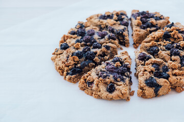 Freshly baked oat blueberry scones on baking paper on white wooden background, close up. Sweet food with natural ingredients. Vegan gluten free pastry.