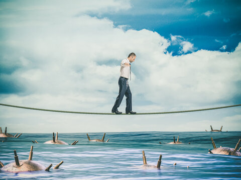 businessman walks on a tightrope over a sea full of mines.