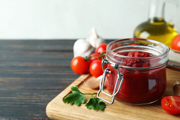 Jar with tomato paste on wooden table with ingredients