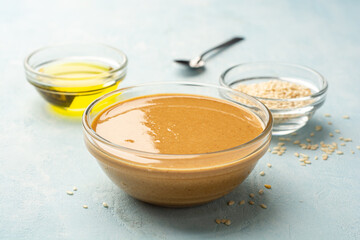 Homemade Tahini sauce in glass bowl with ingredients on concrete background