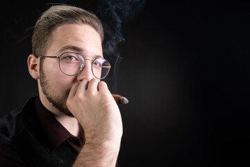 Young handsome man smokes a cigar.