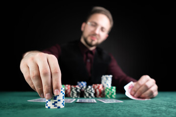 Young handsome poker player sitting at a green gaming table with a lot of chips and good cards.