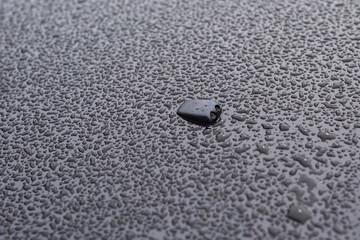 Windshield washer. Black car hood in raindrops