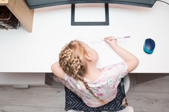 Top view of preschool girl with a wrong posture sitting at the desk, learning to write. Home schooling, education concept