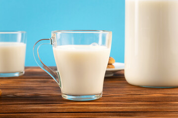 A jug and a glass of milk on a wooden table, on a blue background.