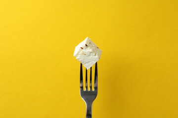 Fork with piece of feta cheese on yellow background