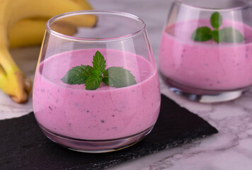 Berry banana smoothie garnished with mint on a marble background.
Close-up.