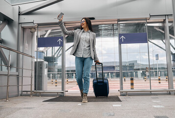 Naklejka premium Happy caucasian woman traveller in airport terminal with luggage
