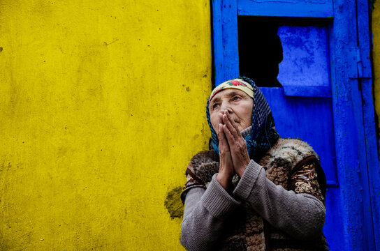 An elderly woman in prayer. Grandmother prays on a yellow background. An old grandmother in a slum. Poor grandmother on a yellow background.Poor grandmother portrait photo.Social disadvantage.Poverty