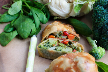 Strudel with broccoli, spinach, carrot, cauliflower and knife on parchment paper