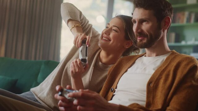 Happy Couple Sitting on the Sofa Playing Video Games, Using Controllers. Competitive Girlfriend and Boyfriend in Love have Fun Playing in Online Video Games at Home Together