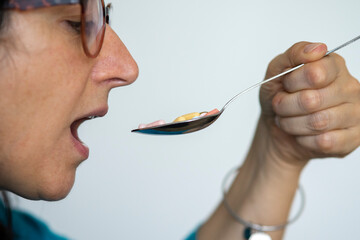 Middle-aged woman takes a spoon full of pills. Concept of drug addiction or need to take many drugs.