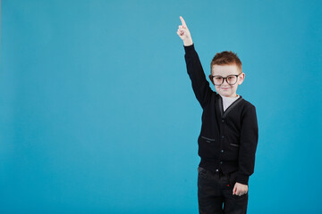 Portrait of stylish little boy with finger pointed up. Little child in glasses has idea. Kid isolated on blue blackboard. Success, bright idea, creative ideas and innovation technology concept.
