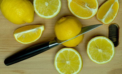 whole lemons and slices of fresh juicy bright yellow lemons laid out on a wooden cutting board with a knife, taken close-up