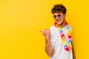 Young caucasian man wearing a Hawaiian party stuff isolated on yellow background points with thumb...