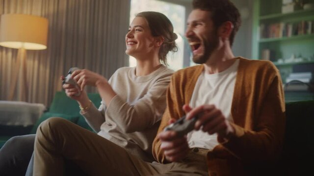 Happy Couple Sitting on the Sofa Playing Video Games, Using Controllers. Competitive Girlfriend and Boyfriend in Love have Fun Playing in Online Video Games at Home Together