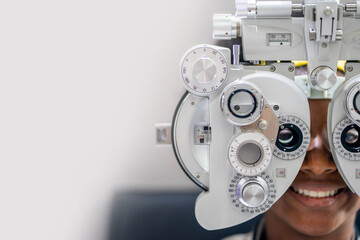 Close-up Of african teen girl Doing Eye Test On Phoropter, African teen girl checking on her eye with optometry machine. copy space background for text - obrazy, fototapety, plakaty