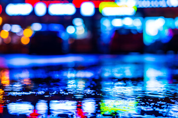 Rainy night. Parking mall with cars. Reflections of shop windows on wet asphalt. Colorful colors. Close up view from the level of the puddle on the asphalt