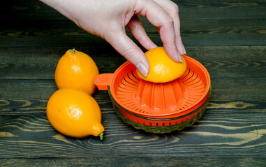 the process of squeezing juice with a hand juicer into a glass cup and two whole lemons on a dark,...