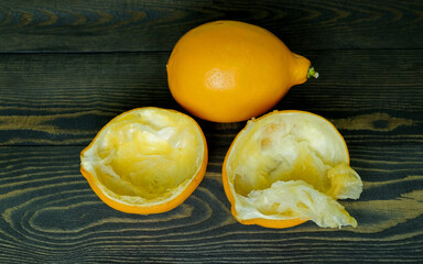 one whole lemon and two halves of squeezed lemon peel on a dark, coarse wooden background from boards