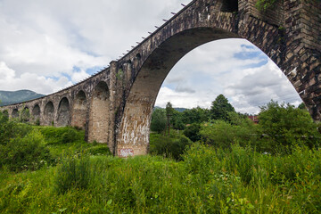 Fototapeta na wymiar Old bridge viaduct in the mountains in summer among green grass and trees.