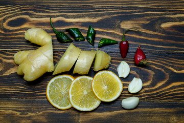 fresh juicy ginger cut into slices, lemon slices, garlic slices, green and red hot peppers on a dark, coarse wooden background