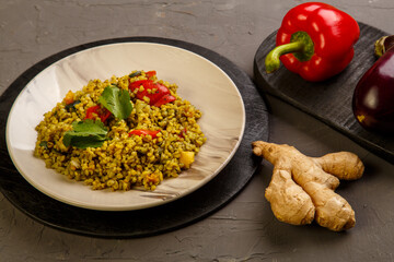 Food for suhoor in Ramadan bulgur post with vegetables in a plate on a gray background near vegetables on a board.