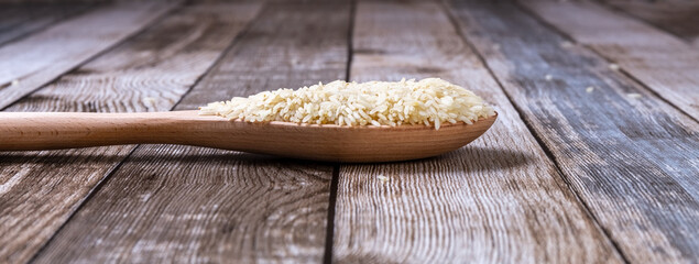 Raw Rice groats are scattered on the table. Rice in a wooden spoon and on a wooden tray. Healthy eating. Diet food. Close-up.