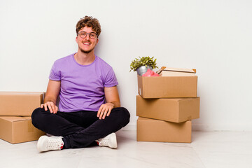 Young caucasian man sitting on the floor ready for moving isolated on white background happy, smiling and cheerful.