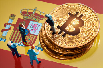 Business meeting about the investment decision for bitcoin concept: Miniature businessman figurines standing near the pile of shiny golden bitcoin on Spain flag.