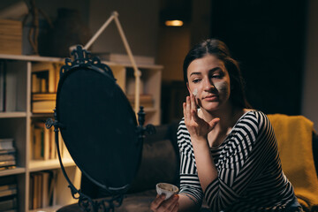 Fototapeta premium woman applying cosmetic face mask at home. evening scene