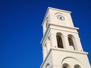 Obraz premium An old bell and clock tower of one of many churches in the village Adamas on Milos island in Greece. It was constructed in a neoclassic architectural style yet maintains the bright white local style.