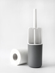 White and gray plastic toilet brush and roll of toilet paper on white background