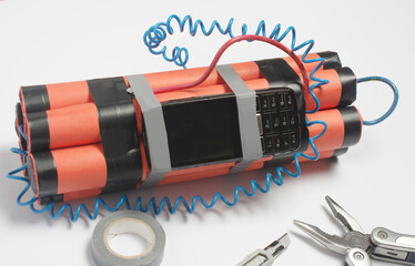 a bomb, a wire tool and an old mobile phone are being assembled on a white table as a timer before the explosion. the concept of terrorism and contract killing.