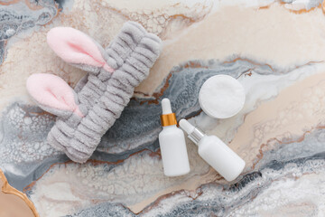 Obraz na płótnie Canvas two white bottle with dropper cap. soft headband with bunny ears. On a marble background. The concept of beauty. Cosmetics for home care.