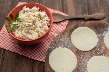 round dough caps and ricotta filling, ham and cheese in a bowl to make homemade pasta with a wooden spoon napkin squared in overhead plane