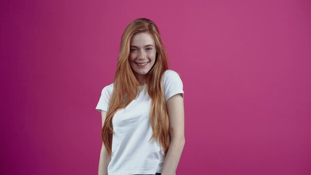 Come to me. The charismatic girl stares forward, and points, you, come here. Freckled teenage girl in a white T-shirt, isolated on a pink background. The concept of people's lifestyle