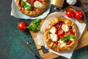 Healthy pastries gluten free, made from rye flour, diet food. Galette tomatoes, mozzarella and basil on a stone background. Top view, flat lay. Copy space.