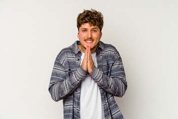 Young caucasian man isolated on white background holding hands in pray near mouth, feels confident.