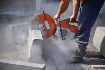 A worker saws a curb with a circular saw, repairs the road, a lot of concrete dust.