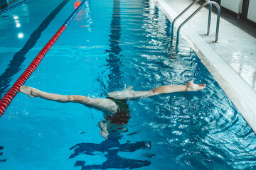 synchronized swimming athlete trains alone in the swimming pool. Training in the water upside down. Legs peek out of the water. sports figure from legs