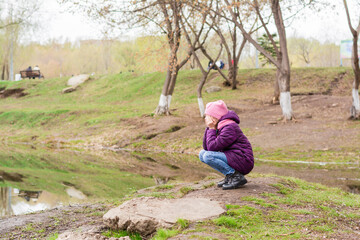 A lonely girl sits and cries covering her face with her hands on the lake in the park. Mental health