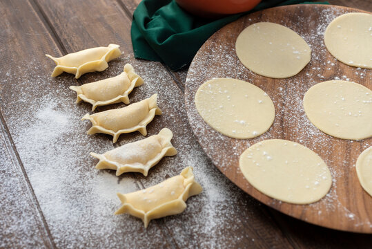 Homemade raw empanadas with repulgue on wooden table and flour with tapas on plate and filling
